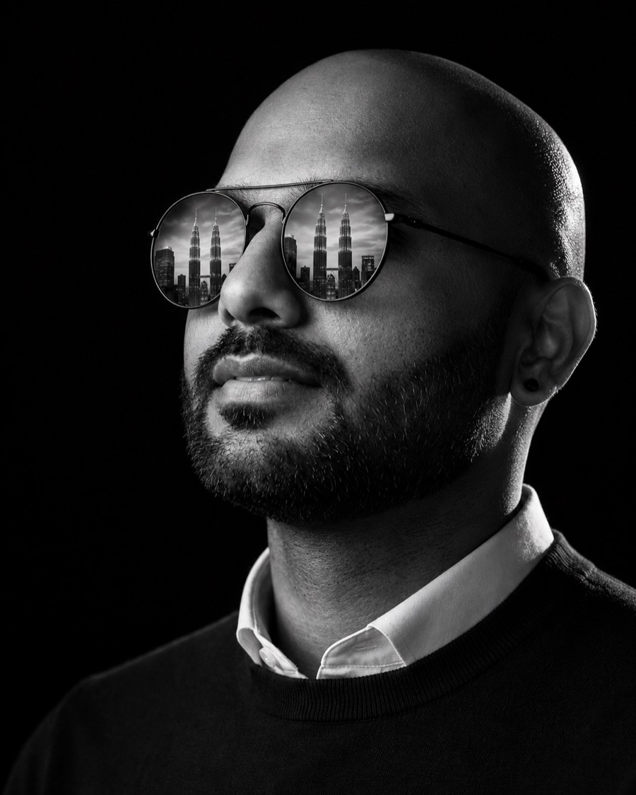 Black-and-white portrait of Dushyanth Ramalingam with the Kuala Lumpur skyline reflected in his sunglasses